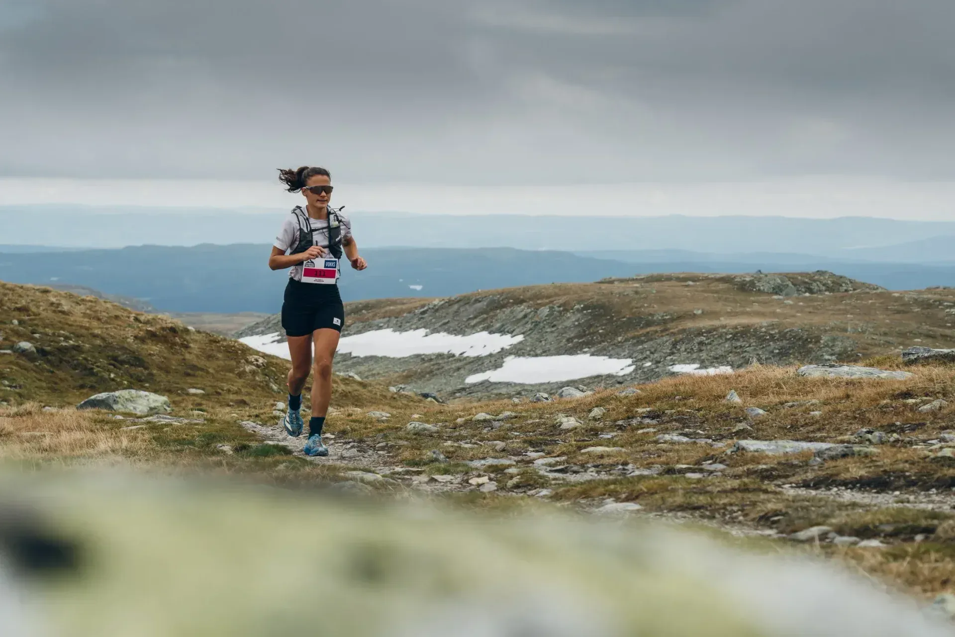 Løper med løpesekk på en steinete fjellsti med snøpartier i bakgrunnen